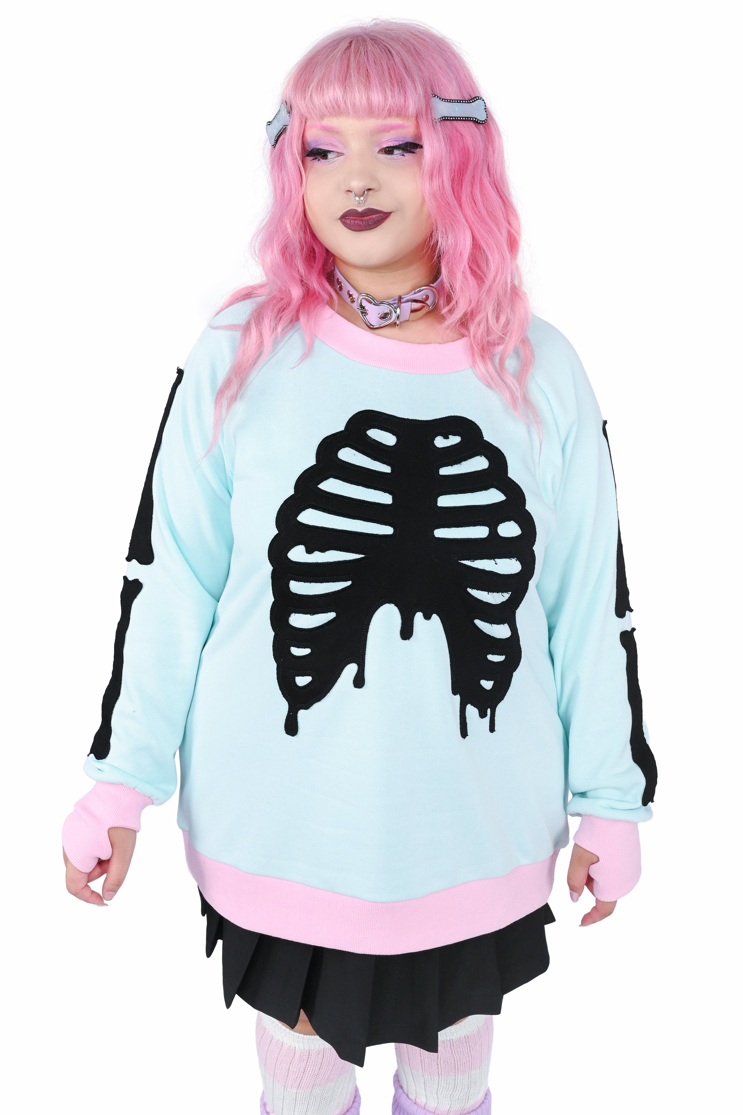Model wearing a mint colored pullover sweater with pink trim and black skeleton appliqué