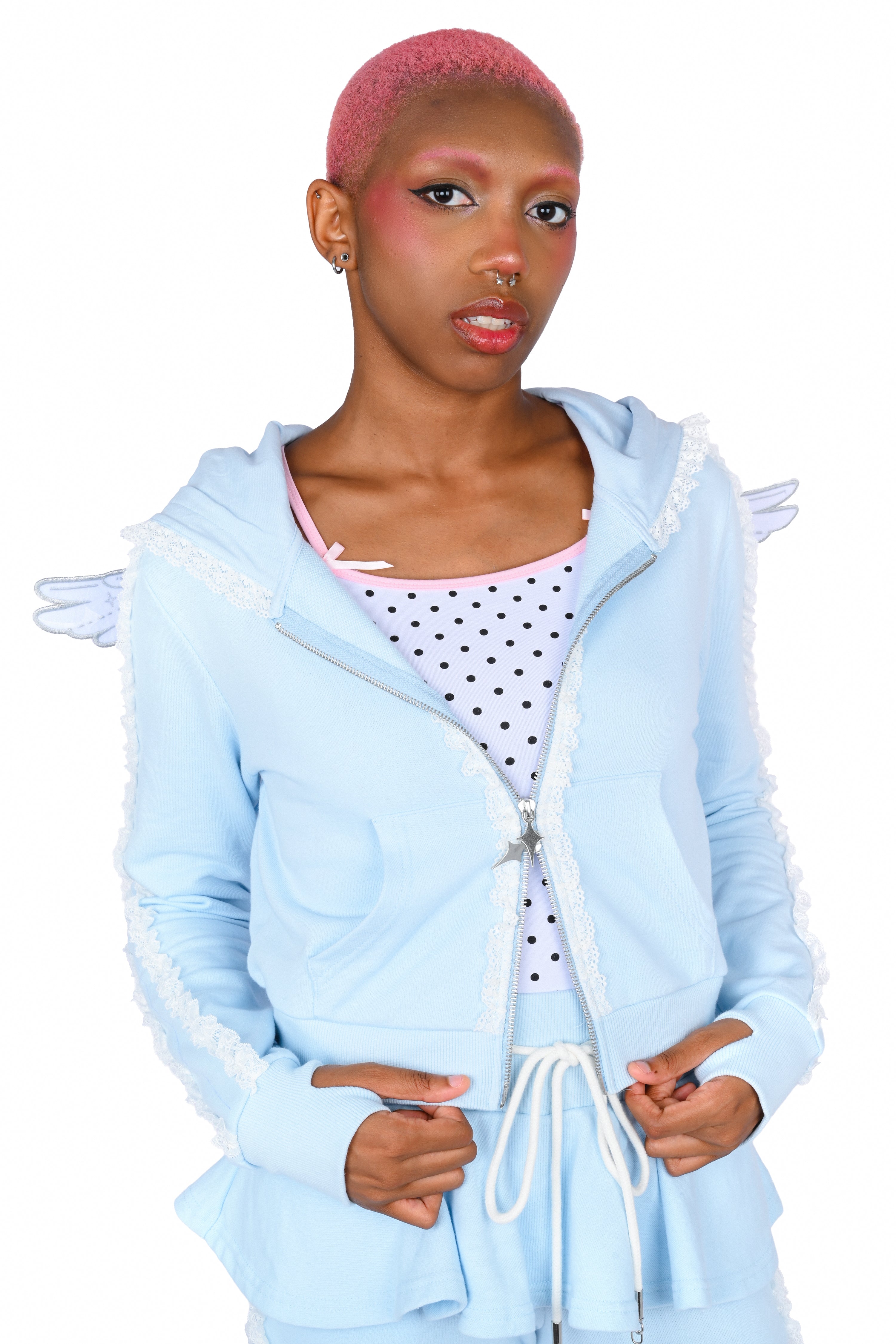 A model wearing a light blue angel-themed zip-up hoodie with white lace trim, white wings, and a white polka-dot top, shot against a solid white background.