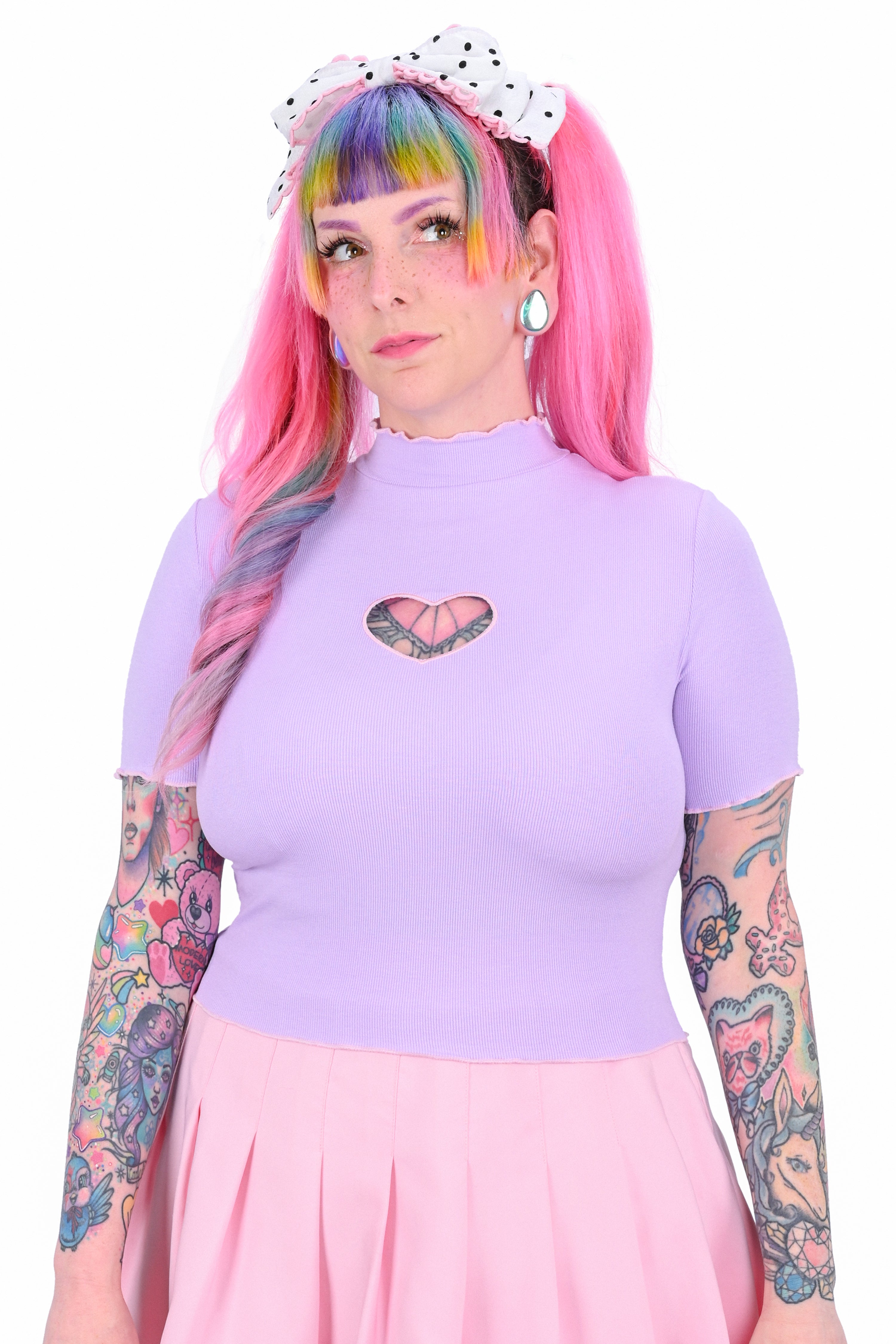 A person wearing a lavender crop top with a heart cut-out at the front, paired with a pink skirt and accessorized with a polka dot hair clip.