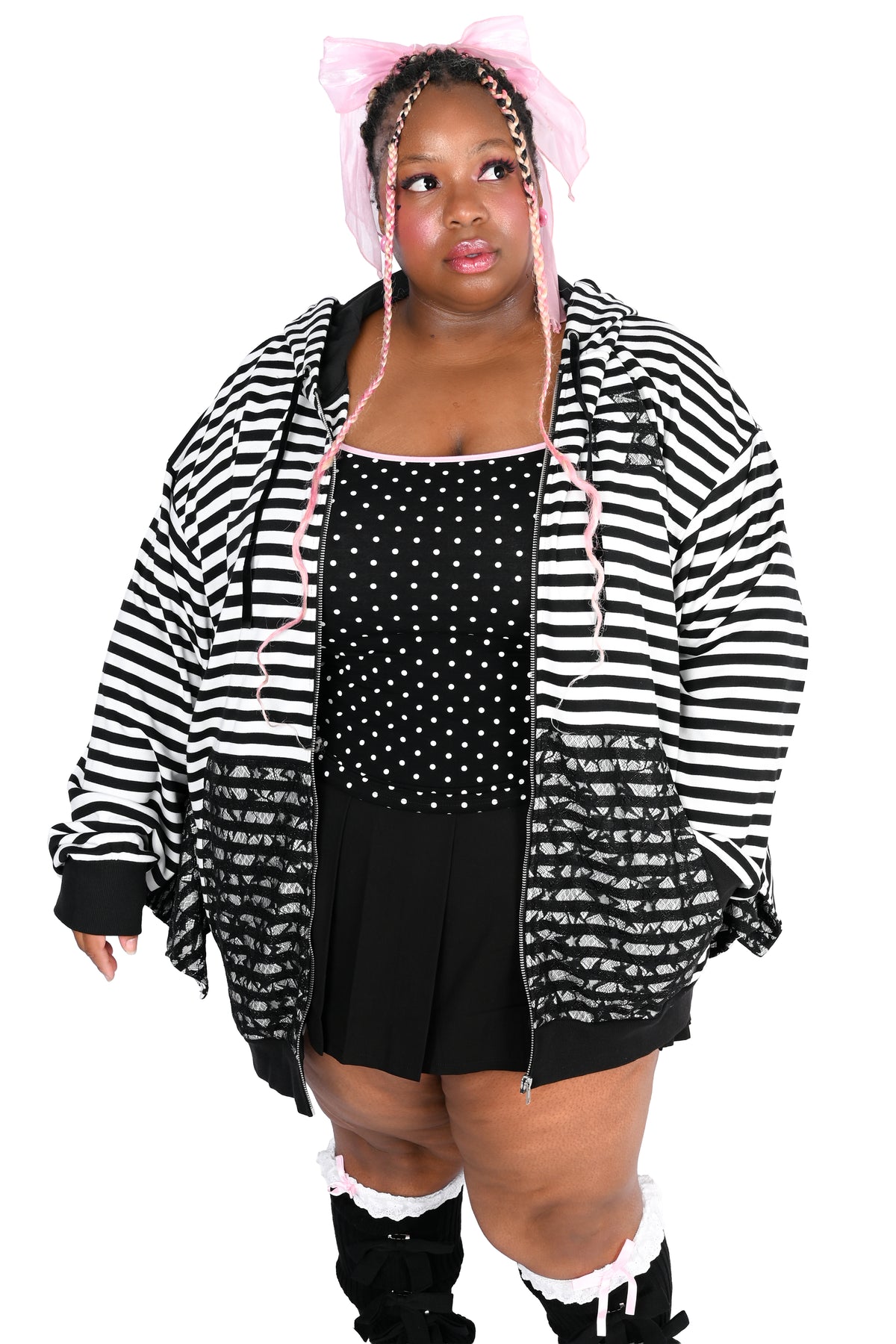 A model wearing a black and white striped zip-up hoodie with lace overlay on the pockets, a black polka-dot tank, a black skirt, and a pink bow headband, set against a plain white background.