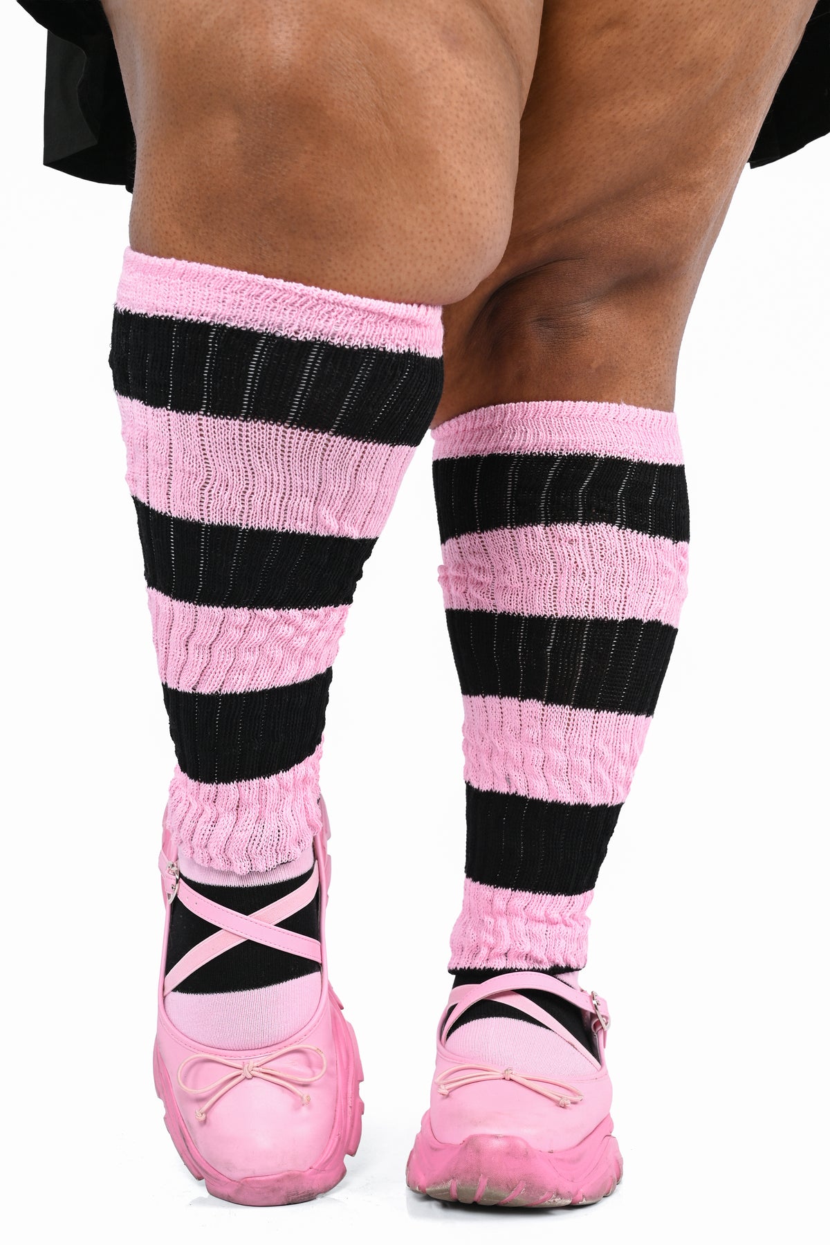 Pink and black striped knee-high socks worn with pink lace-up shoes, shown on a plus model's legs against a white background.