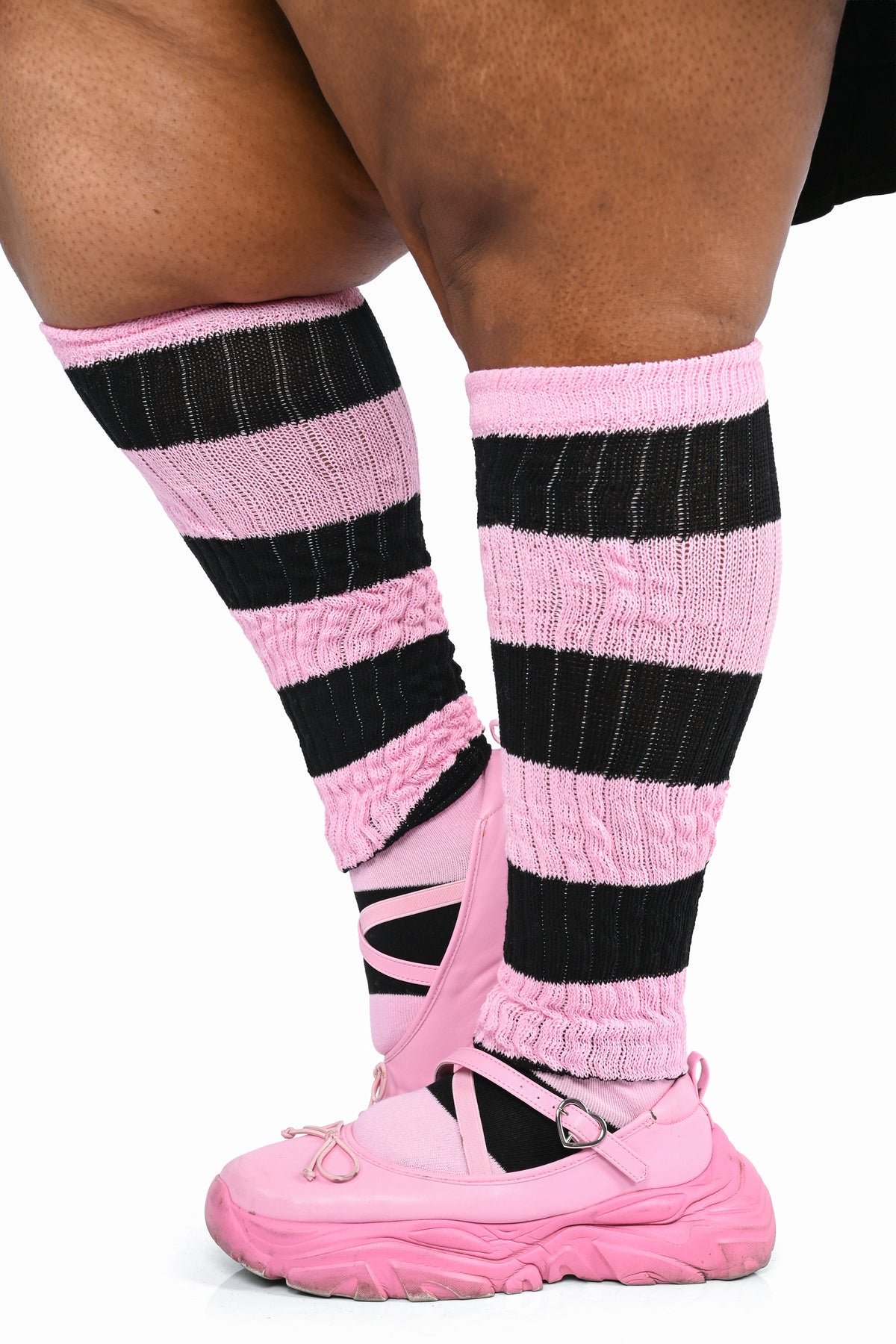 Pink and black striped knit leg warmers worn on legs with pink sneakers, shown against a plain white background.