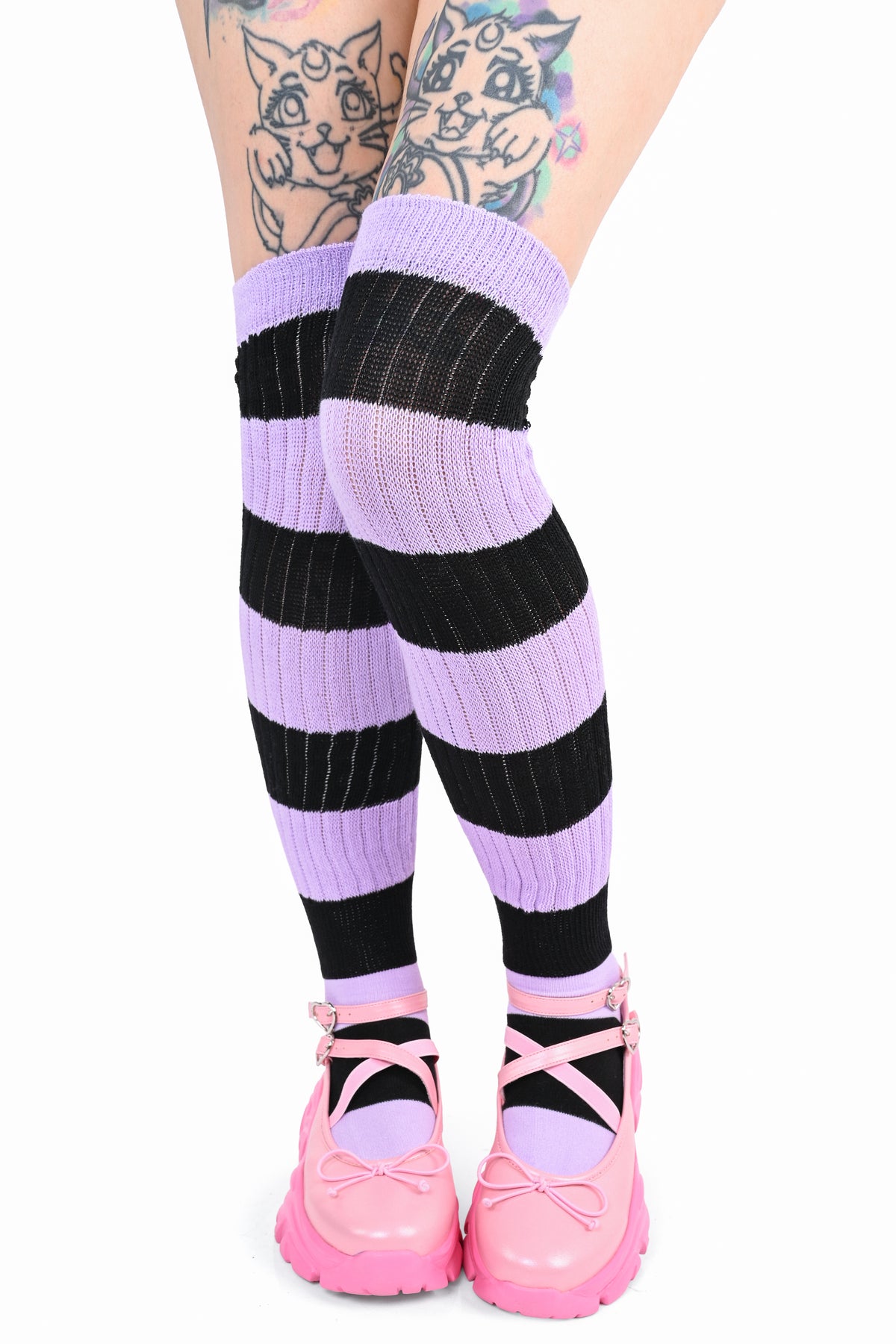 A person's legs wearing purple and black striped otk ribbed socks with pink platform shoes, shown against a plain white background.