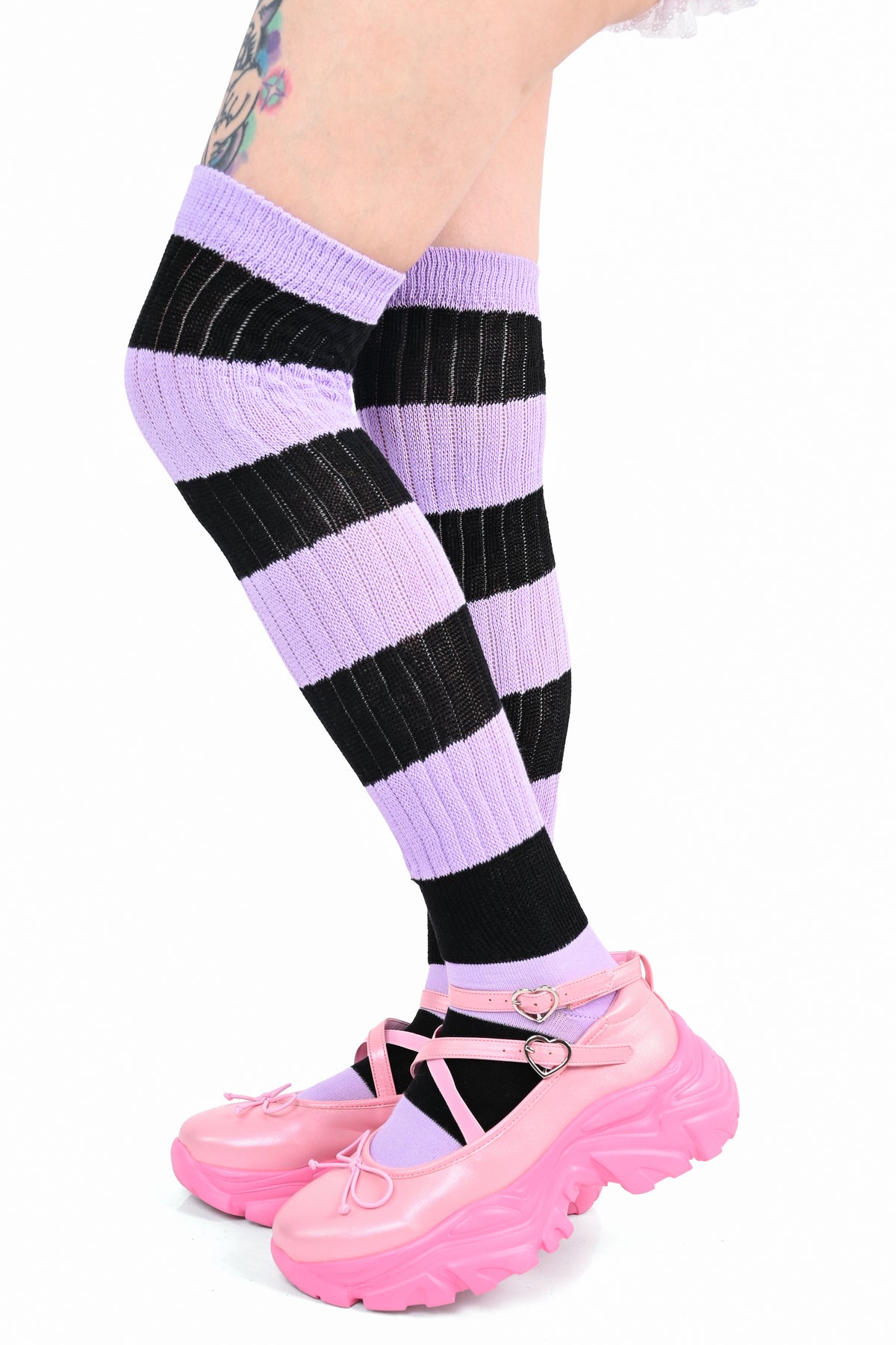A person's legs wearing lavender and black striped knee-high ribbed socks with pink Mary Jane platform shoes, shown against a plain white background.