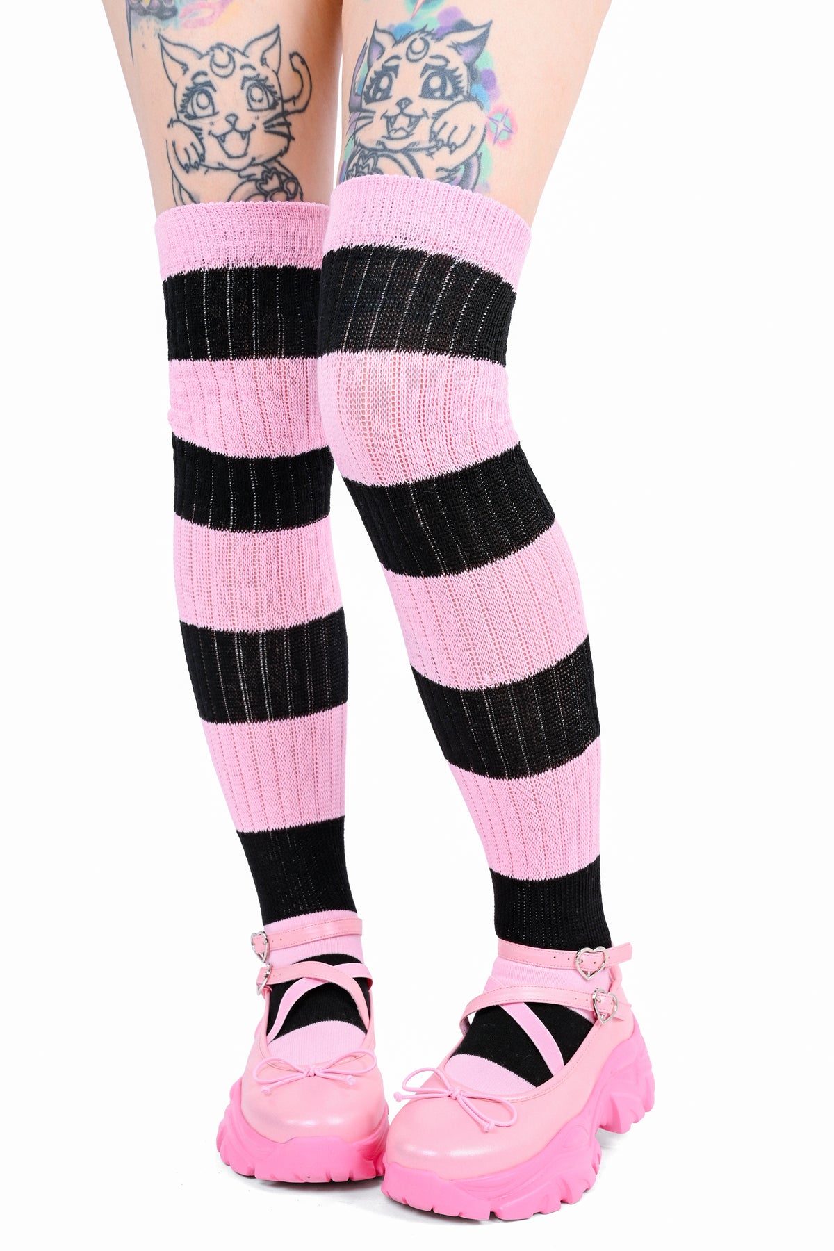 Pink and black striped thigh-high ribbed socks worn by a model, paired with pink Mary Jane platform shoes against a white background facing front