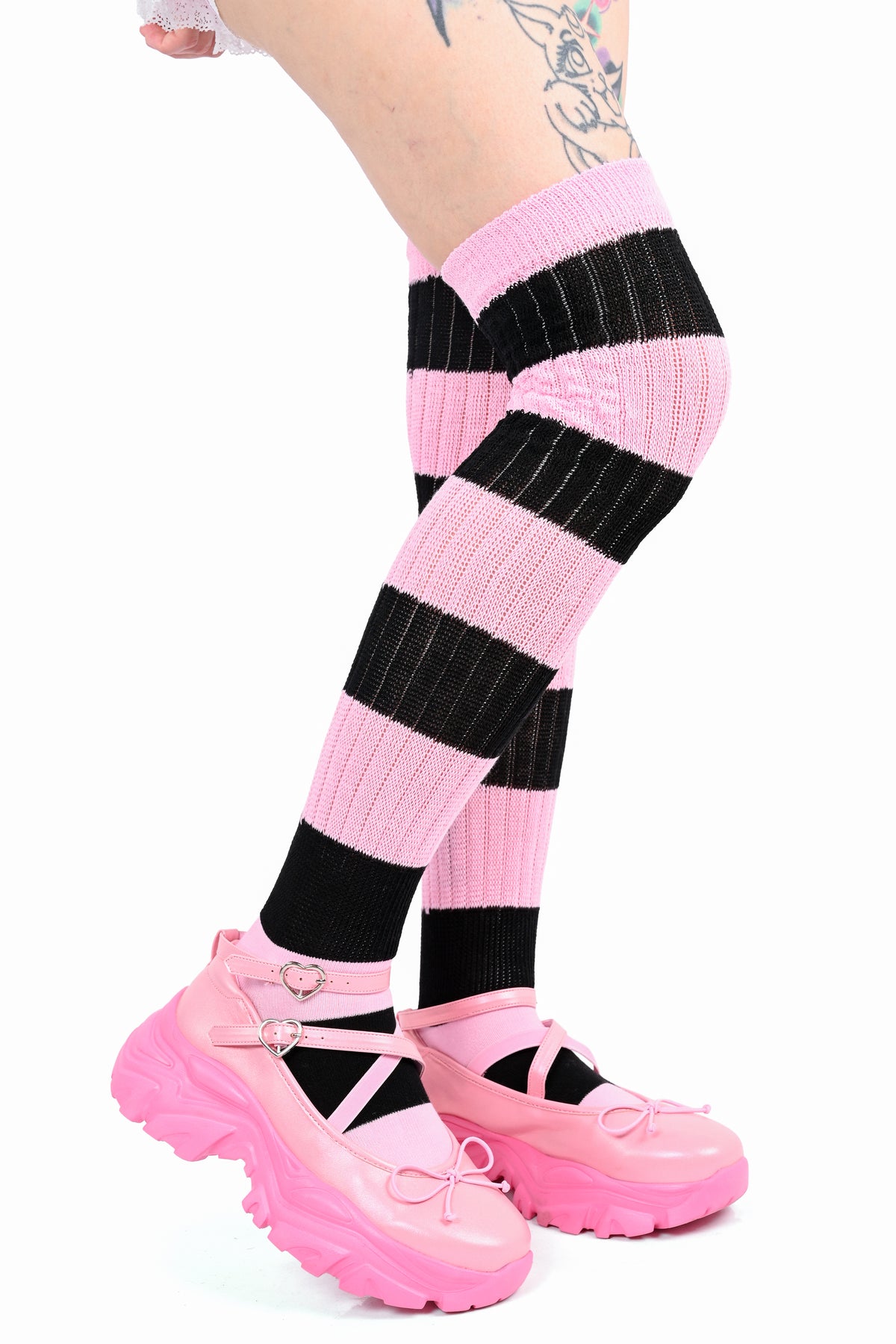 Pink and black striped knee-high ribbed socks worn with pink Mary Jane shoes on a white background. facing side