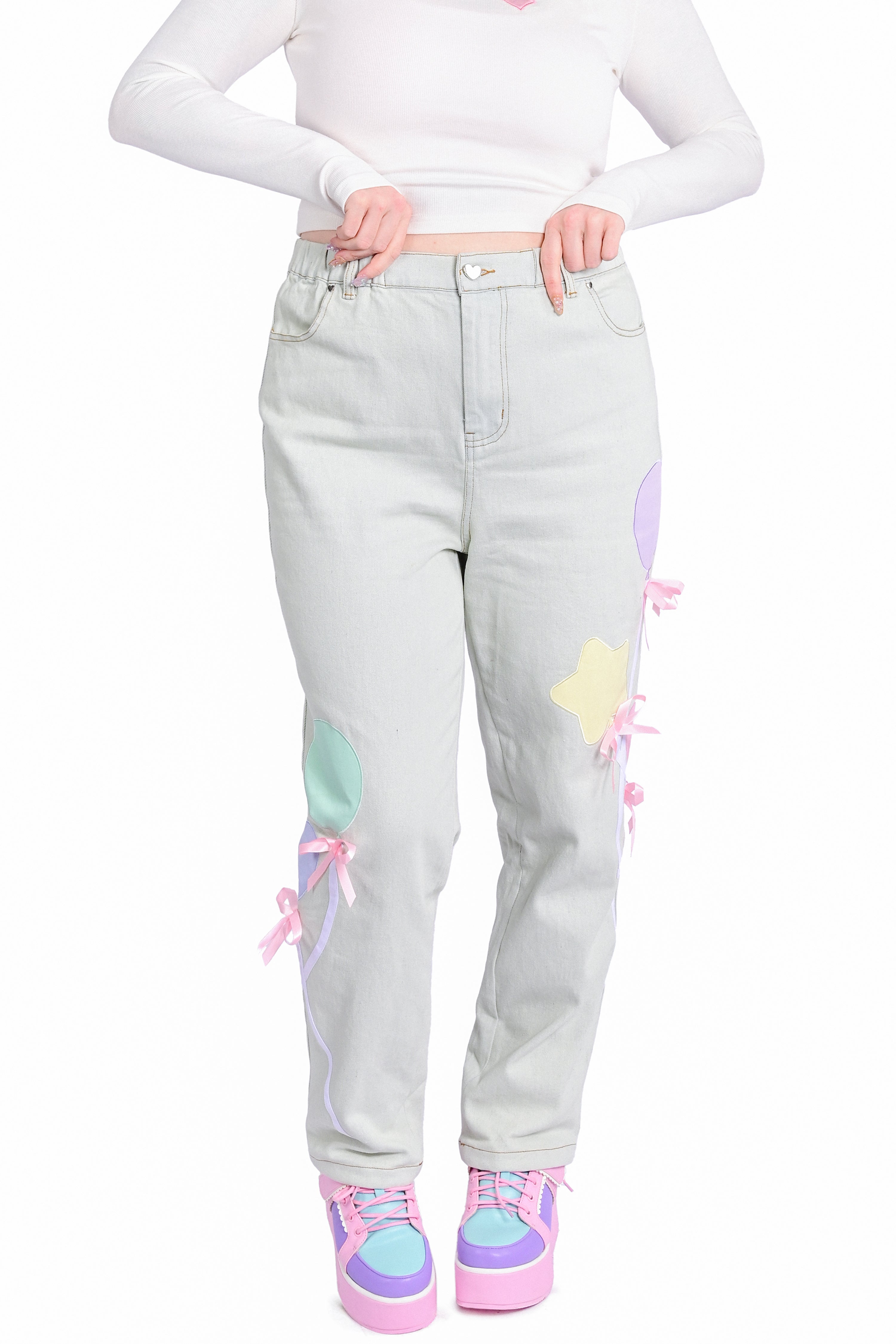 A model wearing a pair of light wash denim jeans with pastel balloon appliques and pink bows.