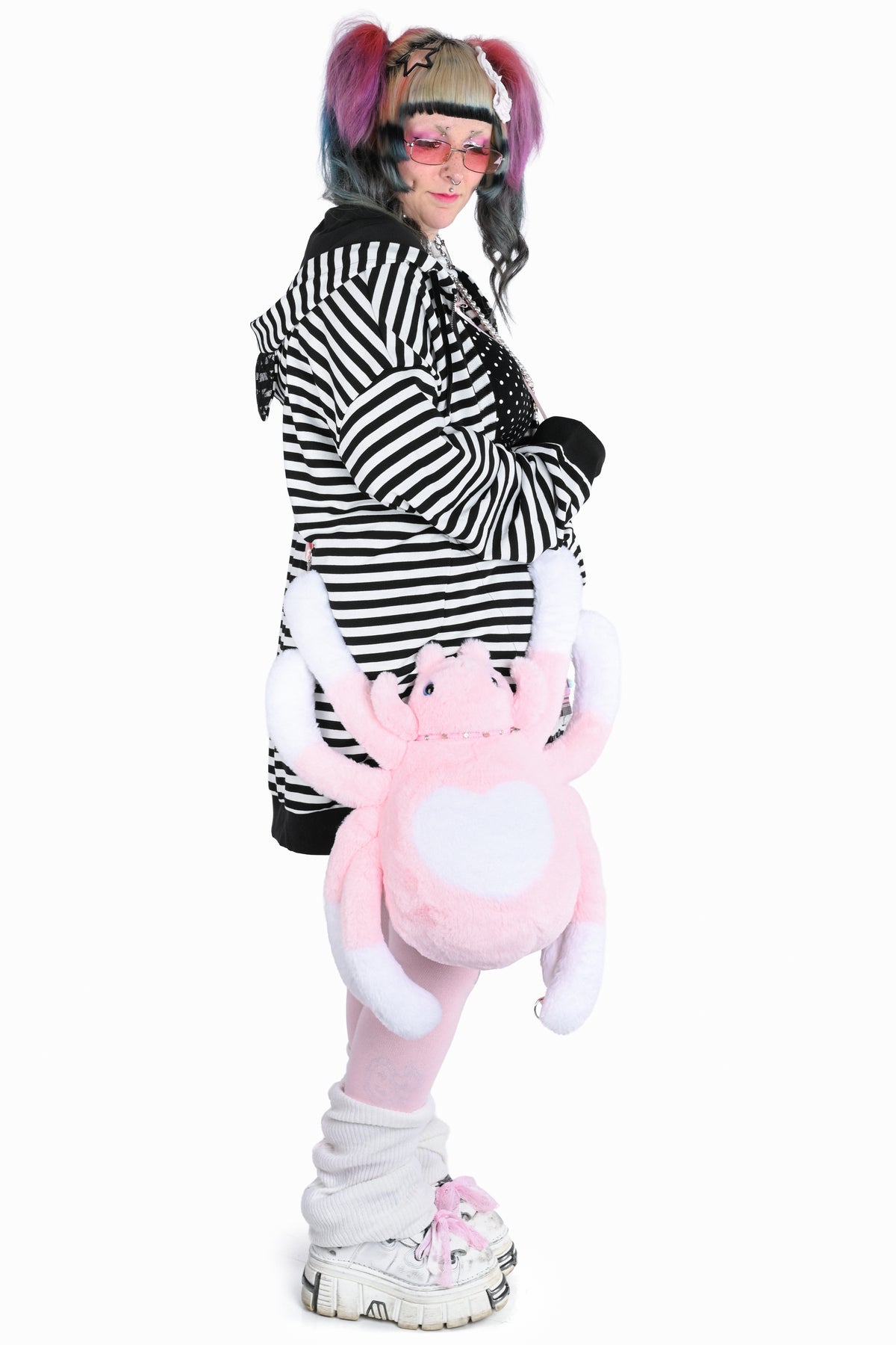 Side view of a model in a black and white striped hoodie wearing a pink and white spider plush as a crossbody bag.