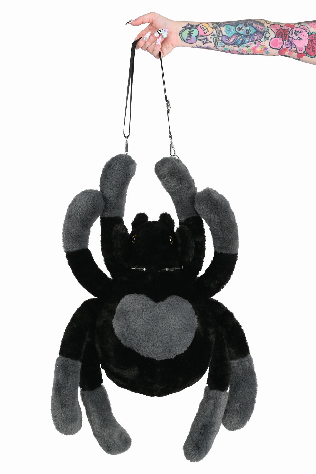 Hand holding a black and grey spider plush bag from the strap.