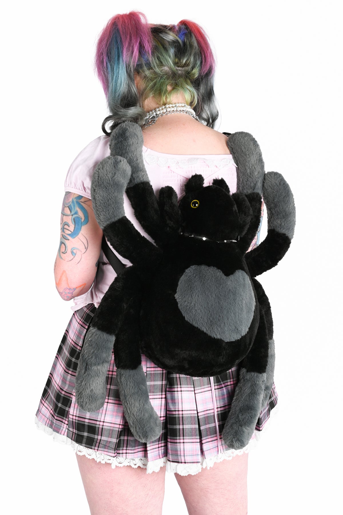 Back view of a model in a pink outfit with a large black and grey spider plush bag worn as a backpack.