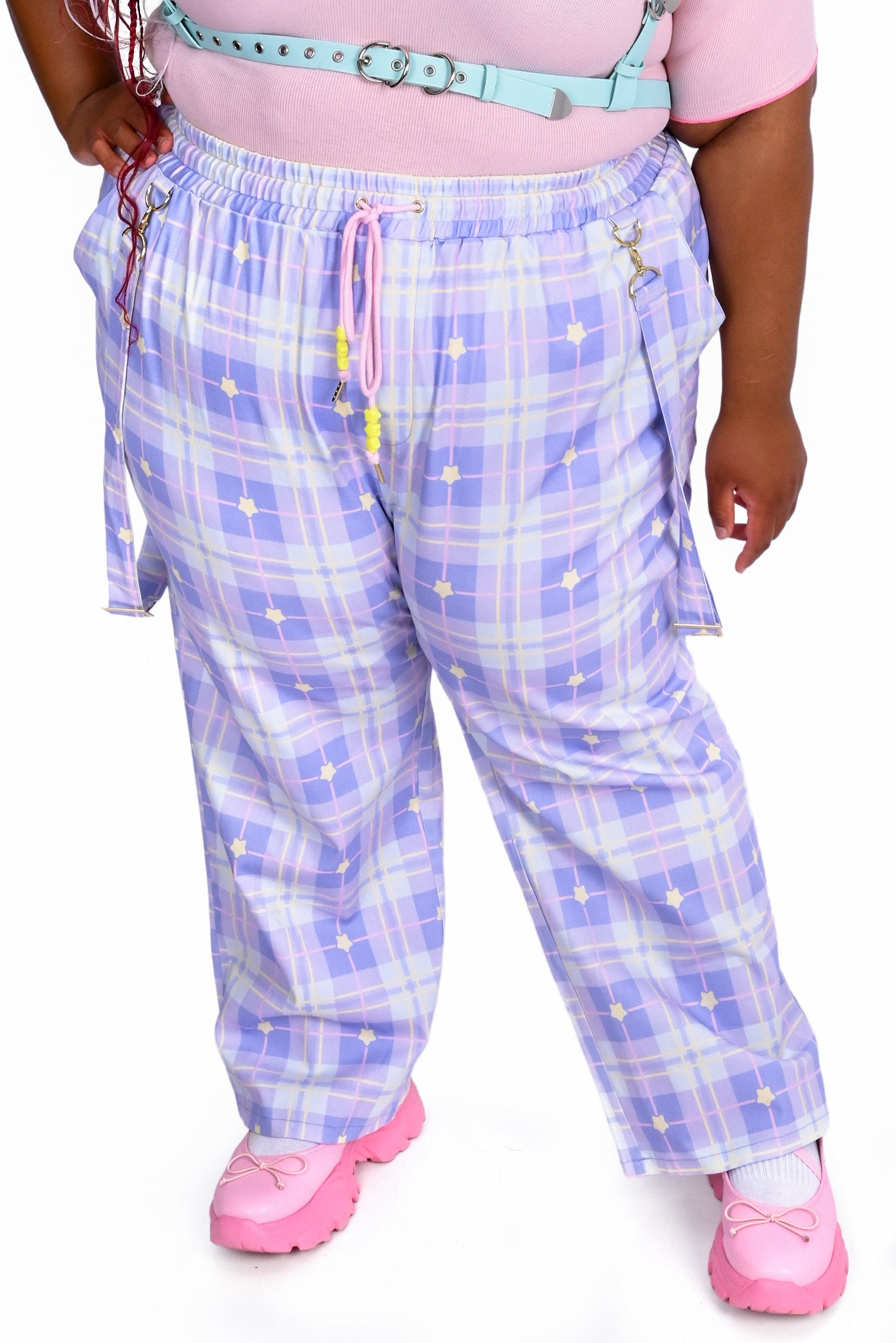 Person wearing a pink top and blue plaid pants on a white background