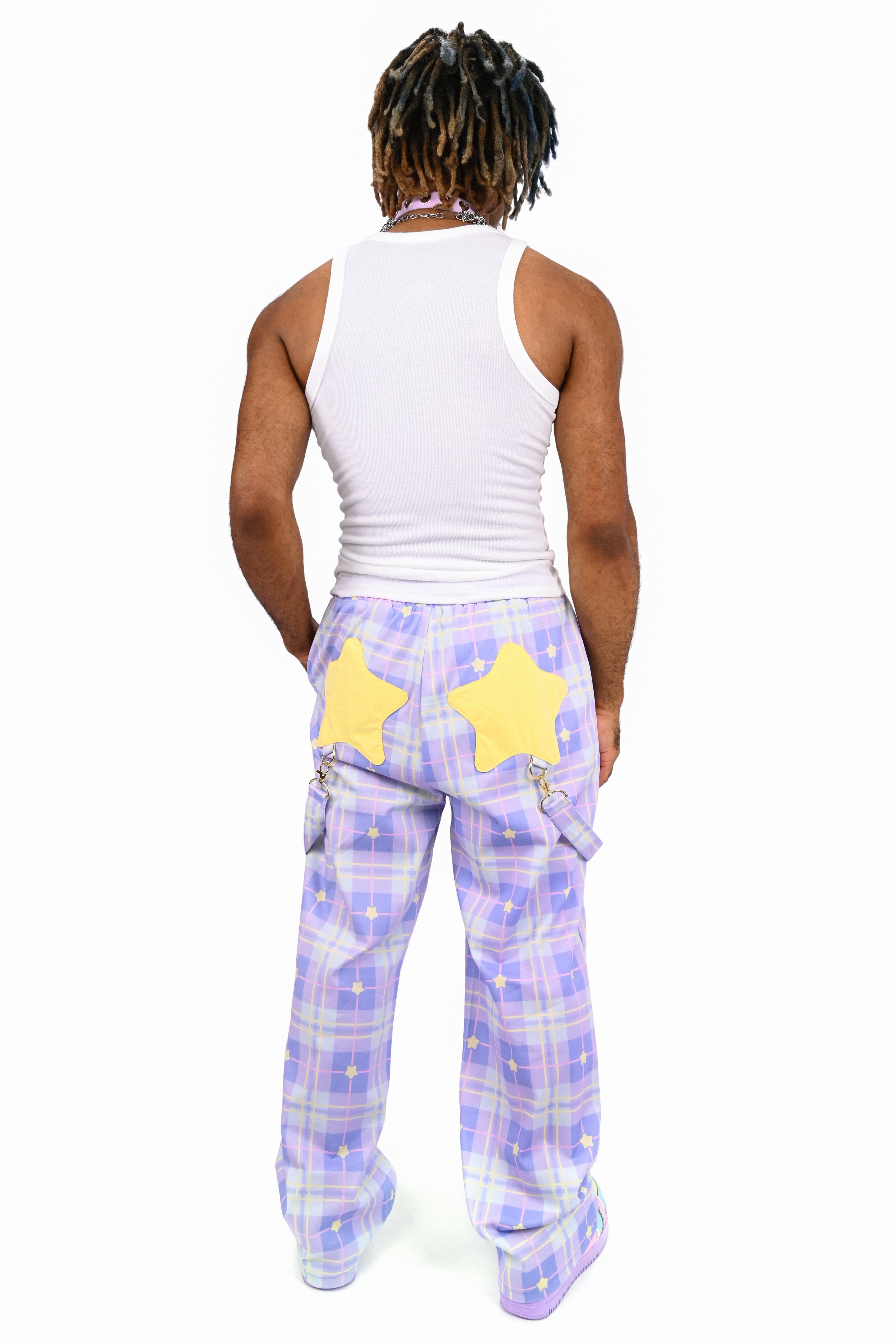 Person wearing a white tank top and purple plaid pants with yellow stars on a white background