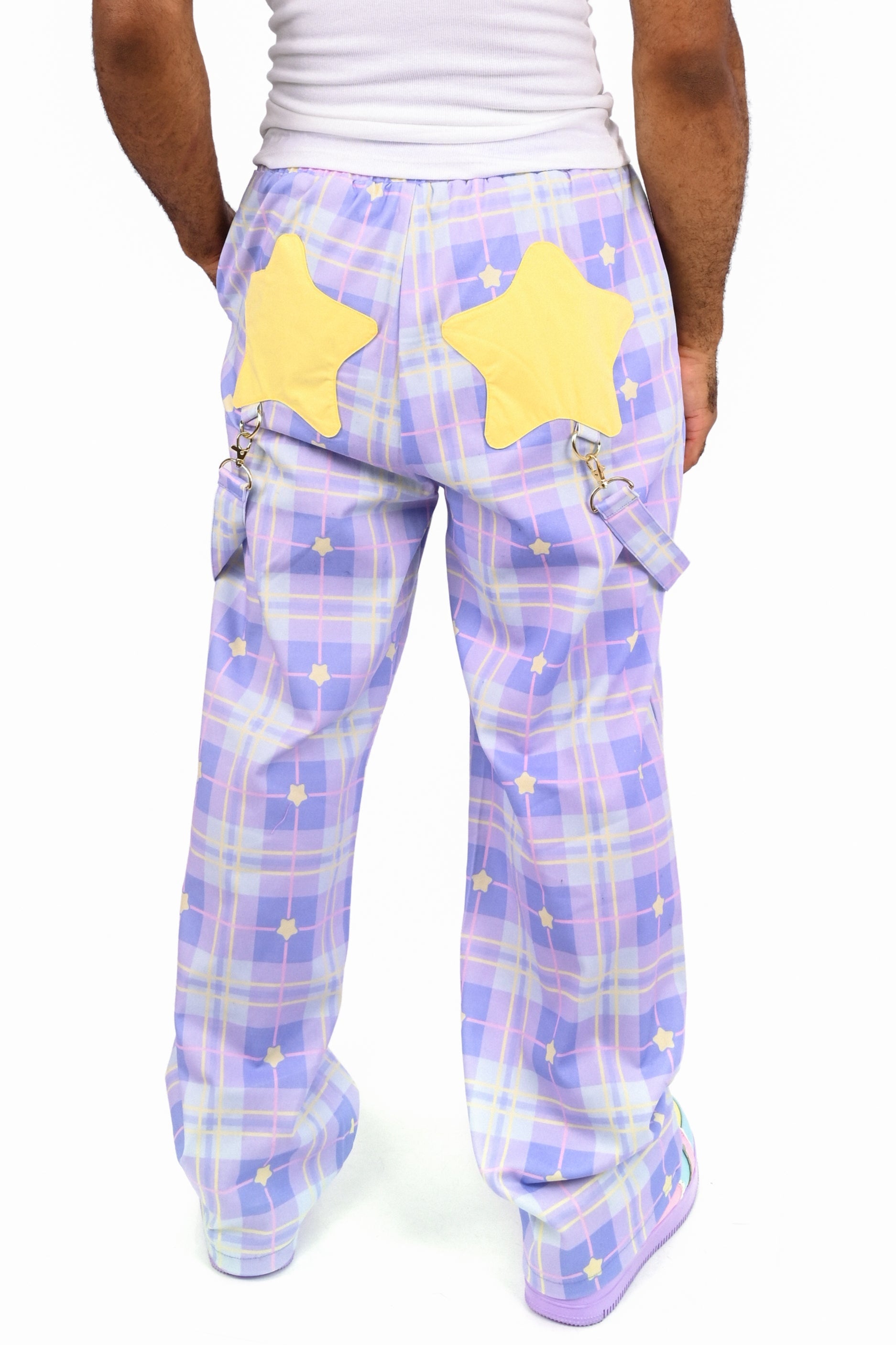Person wearing a white tank top and purple plaid pants with yellow stars on a white background