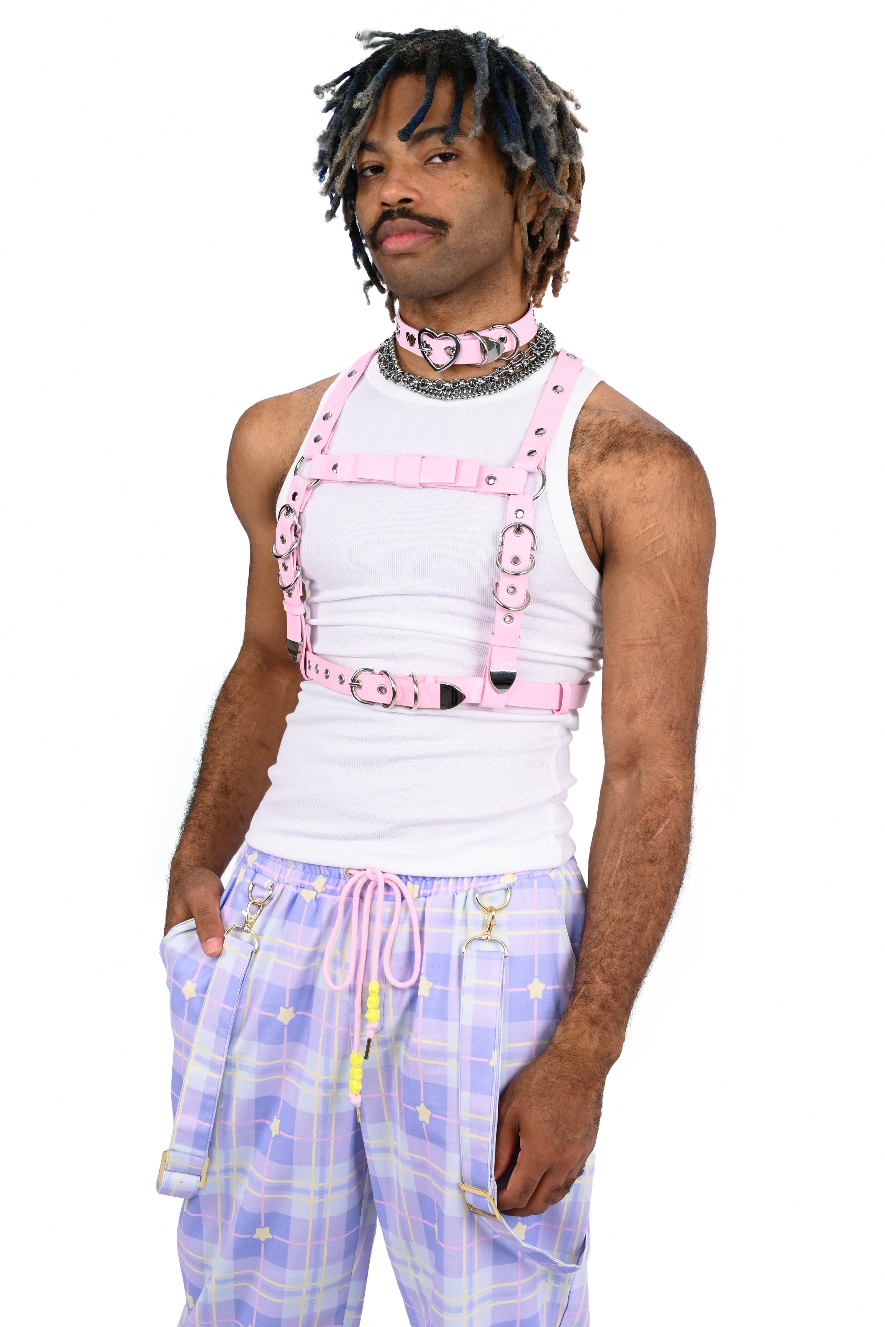 Person wearing a white tank top with pink suspenders and plaid pants on a white background