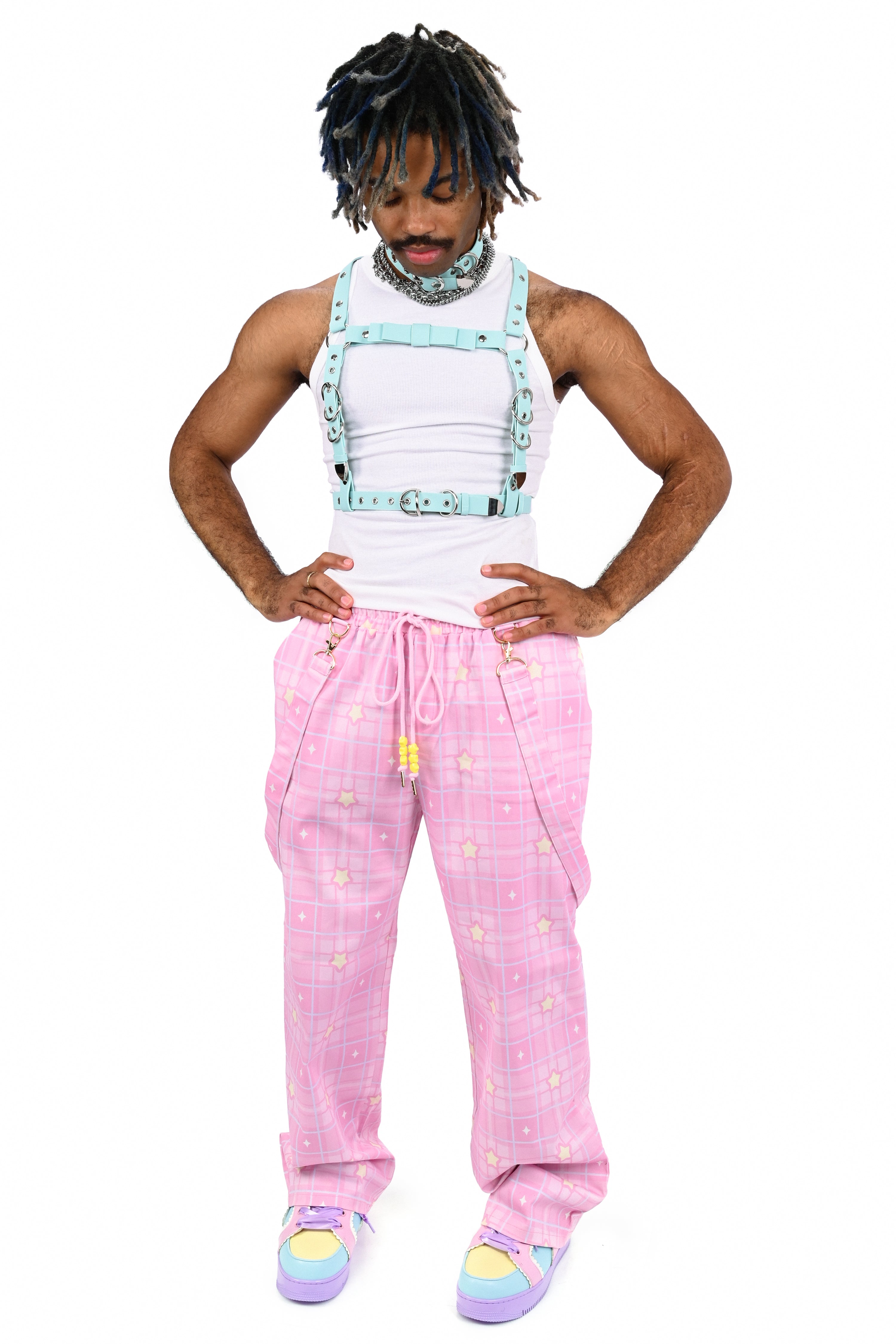Person wearing a white tank top, pink checkered overalls with suspenders, and colorful socks on a white background
