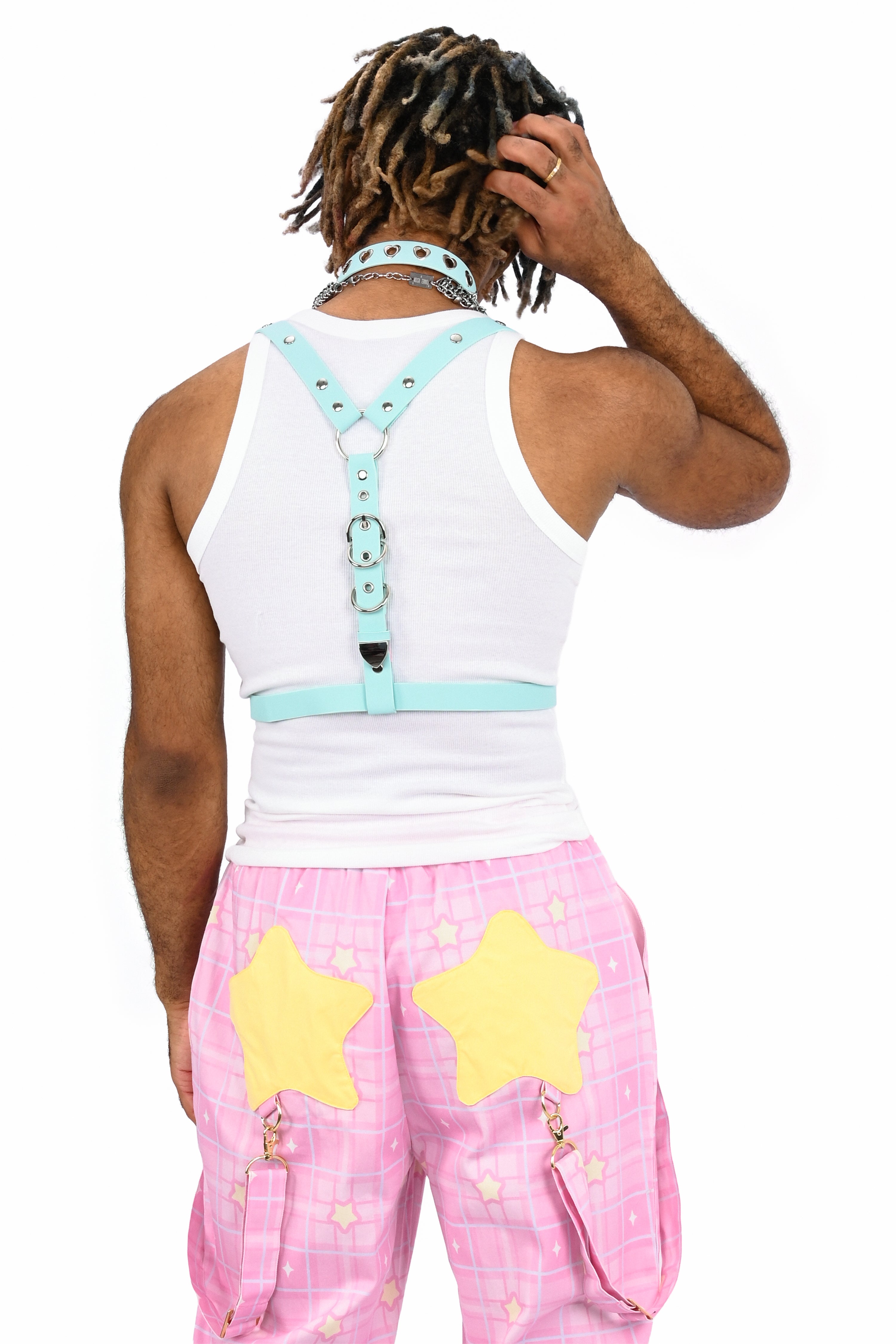 Person wearing a white tank top with a light blue harness and pink pants with yellow stars on a white background
