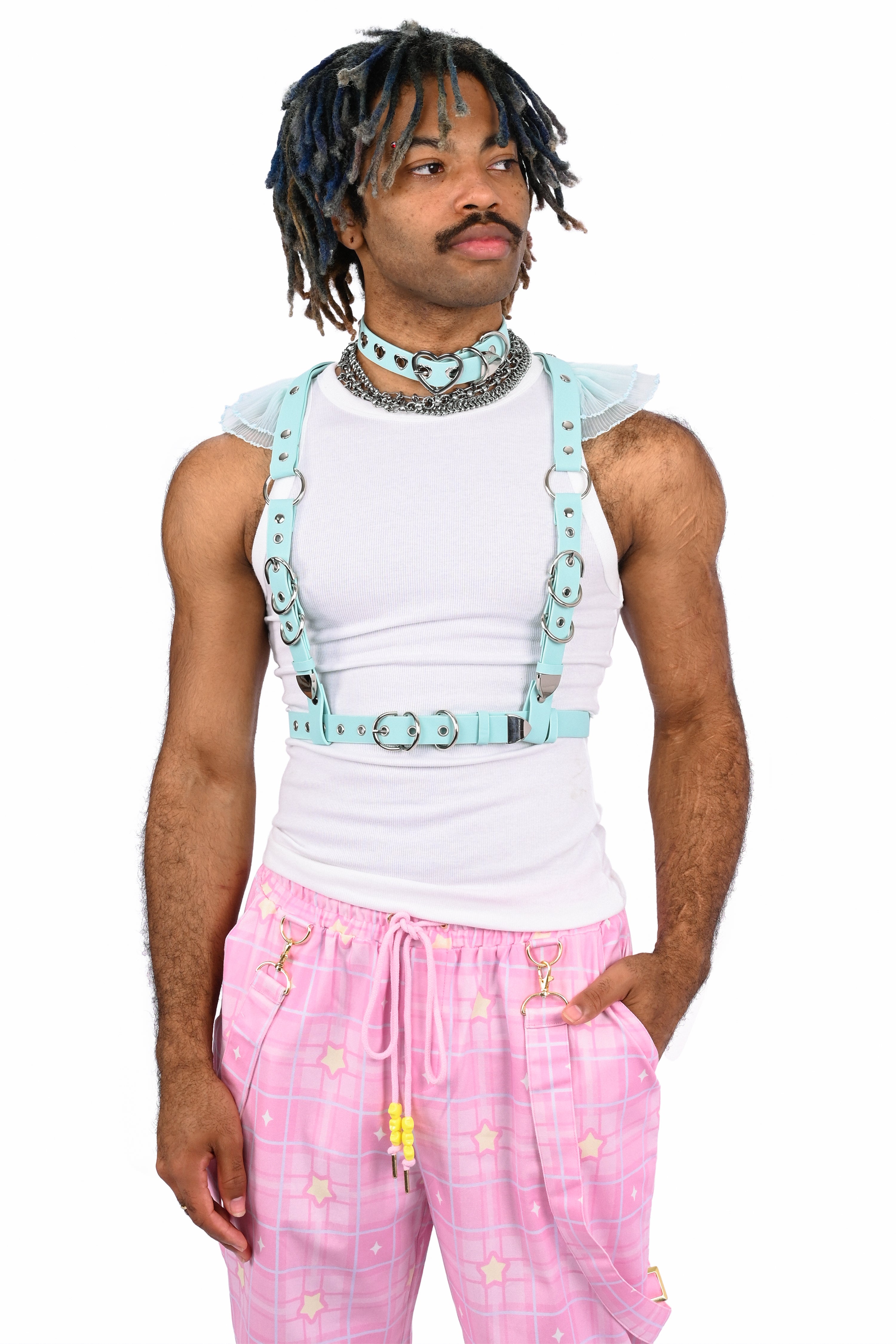 Person wearing a white sleeveless top with blue suspenders and pink pants on a white background