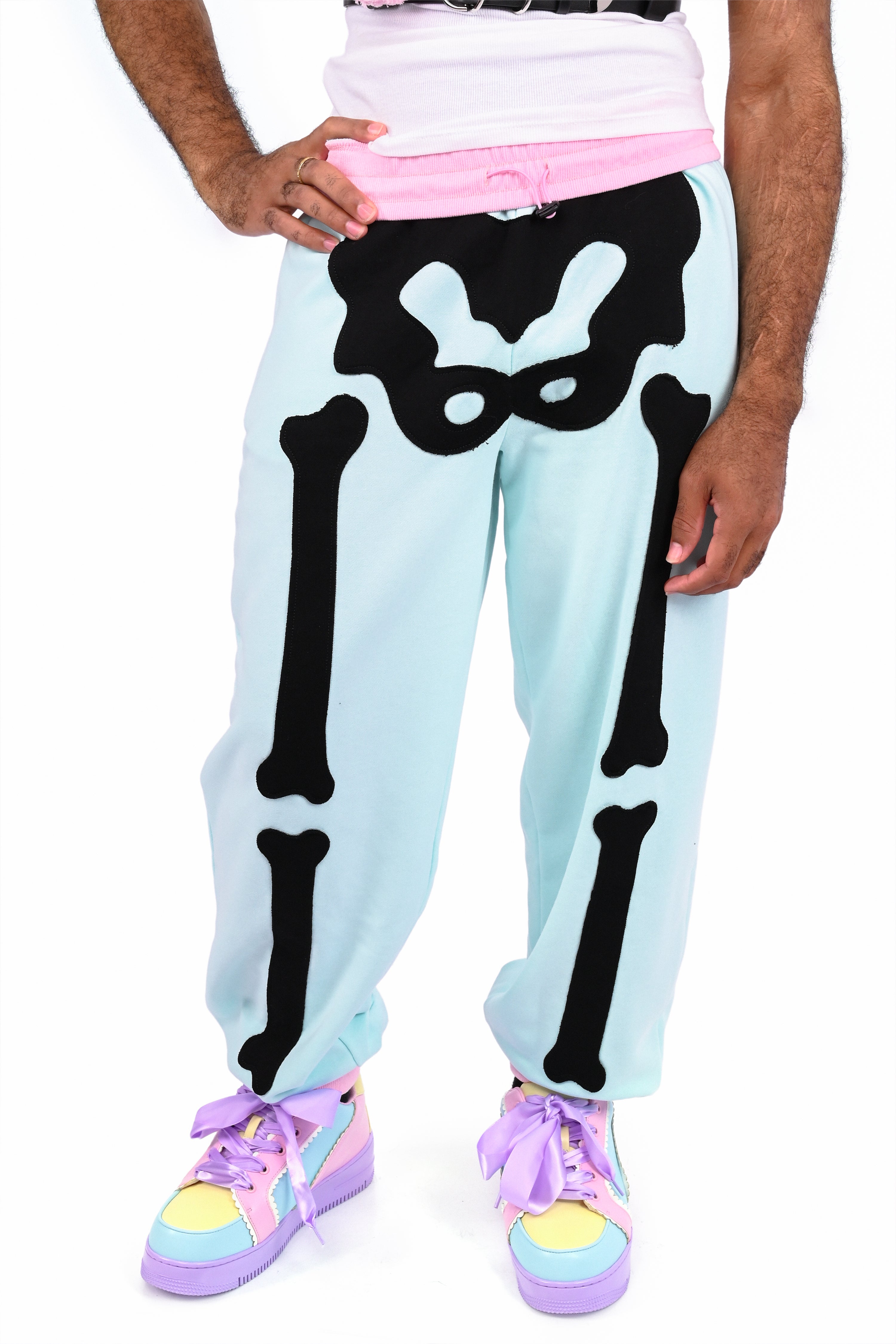 Model wearing a pair of mint colored sweatpants with pink trim and black skeleton appliqué