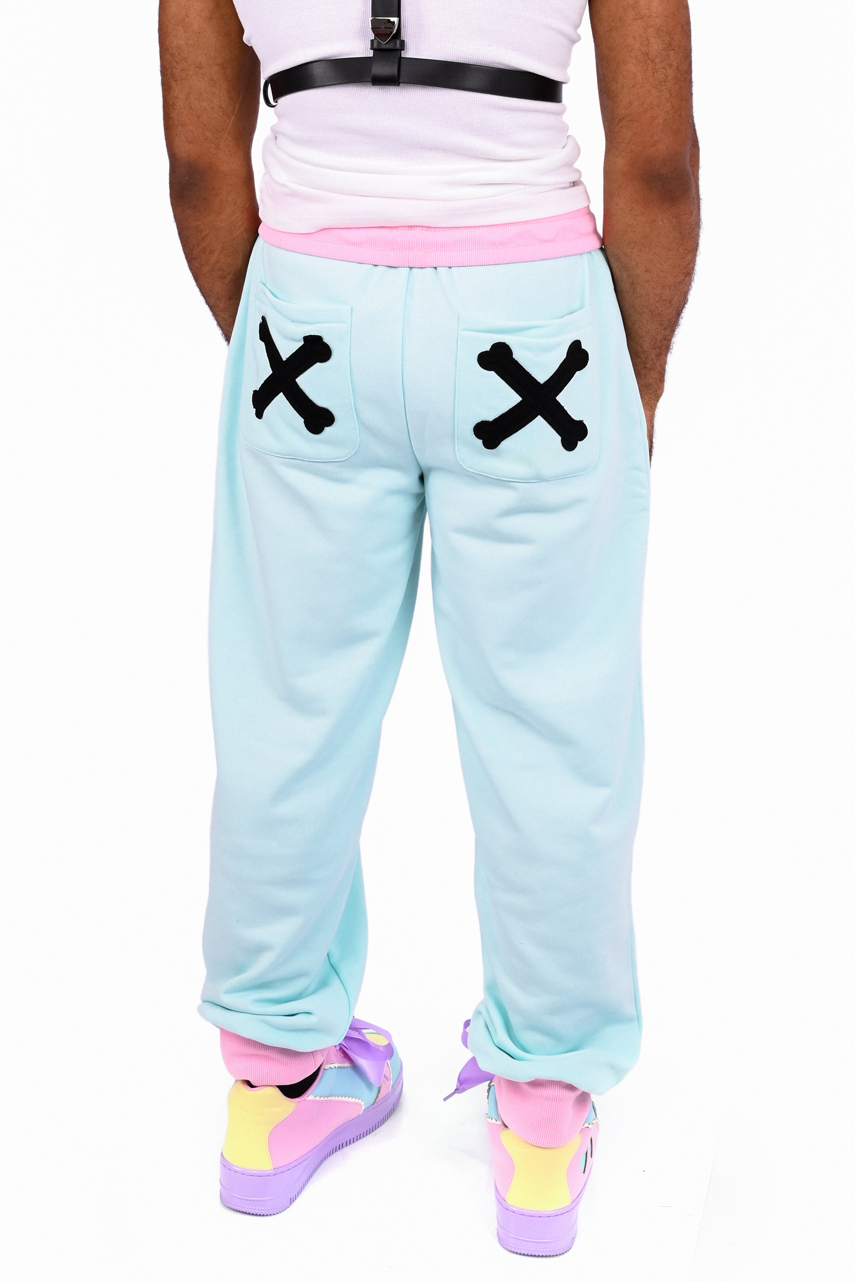 Model wearing a pair of mint colored sweatpants with pink trim and black cross-bone appliqué on the back pockeets