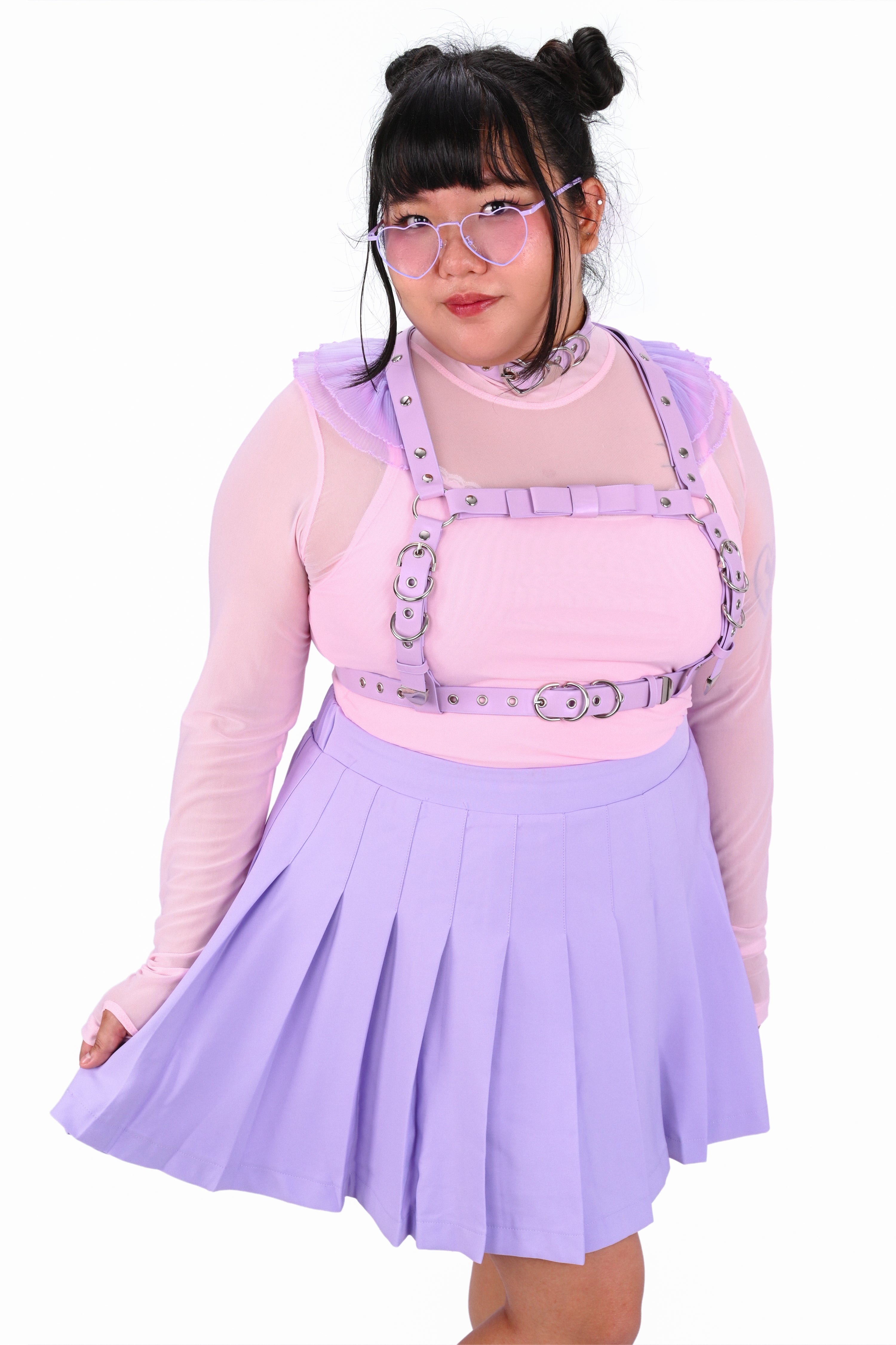 Person wearing a pink top with suspenders and a purple pleated skirt on a white background