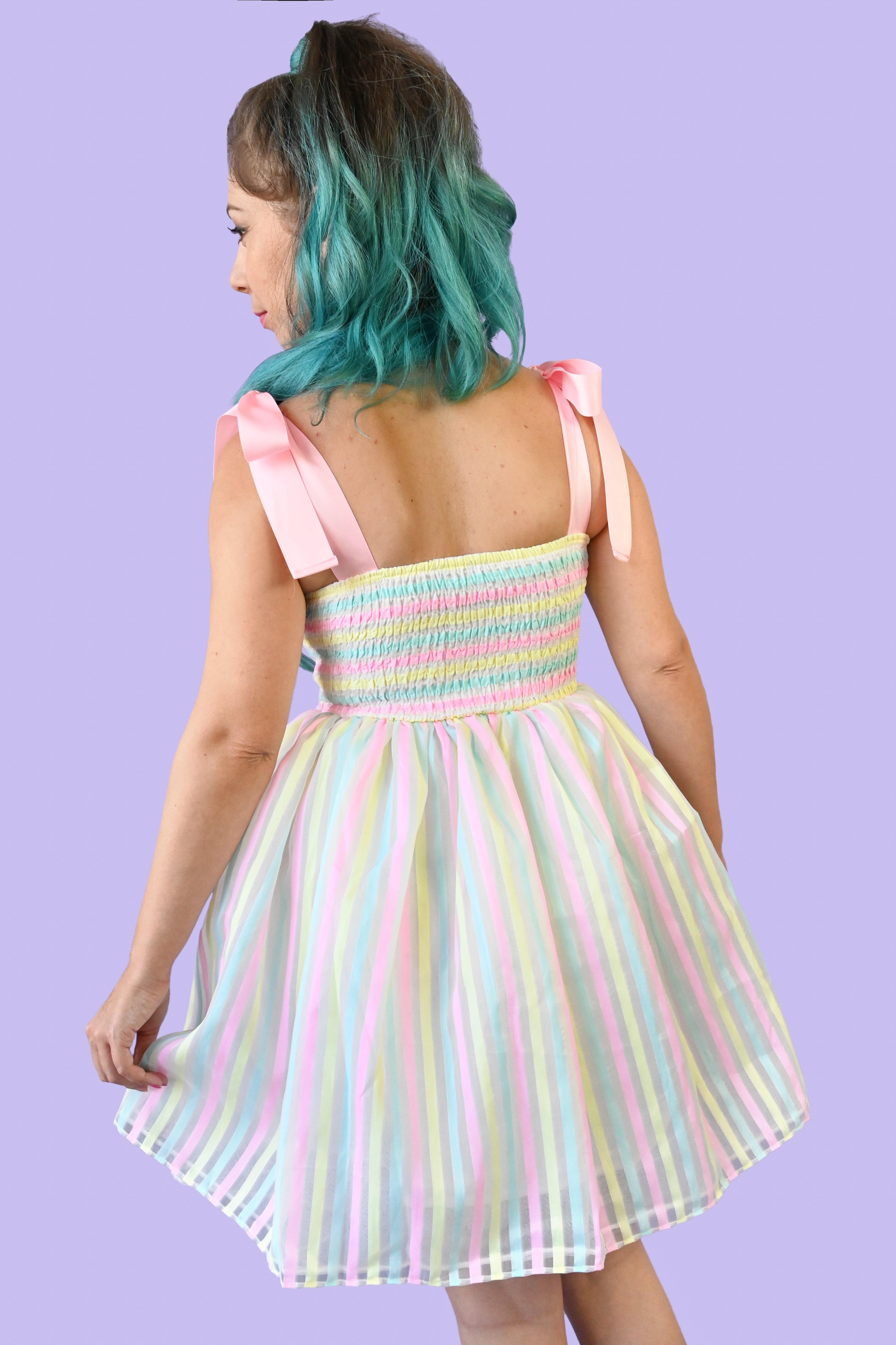 Back view of the dress. Pink ribbon straps, horizontal pastel yellow, blue, and pinkstripes on a shirred bodice and a cupcake style sheer vertical striped skirt over a white slip